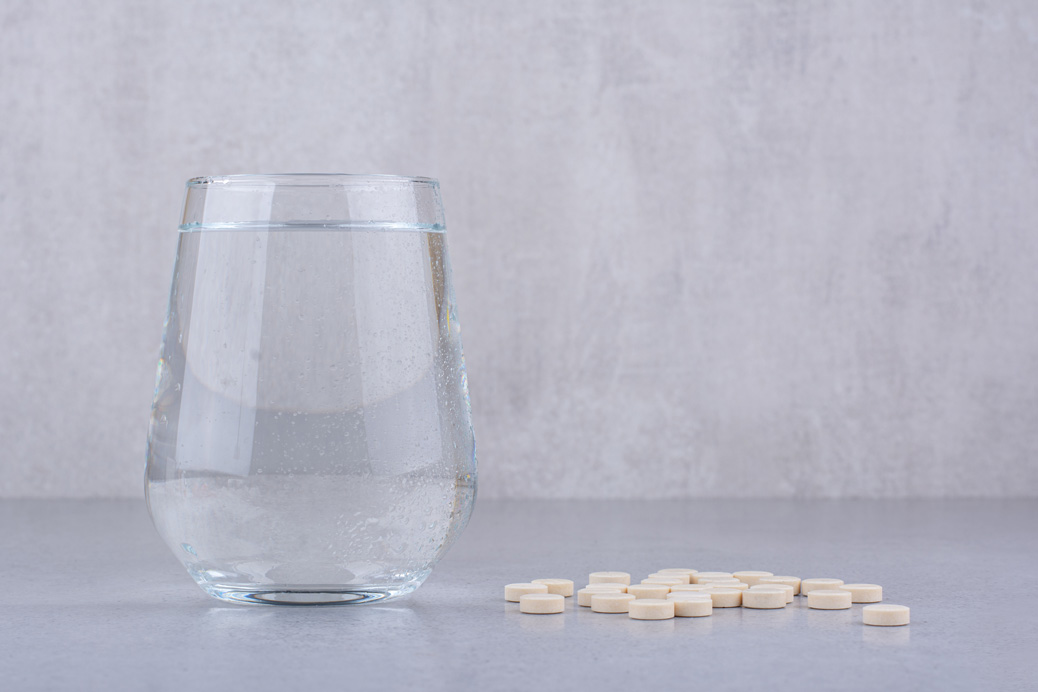 Szklanka wody z leżącymi obok tabletkami – symbol farmaceutyków trafiających do środowiska wodnego i ich biodegradacji
